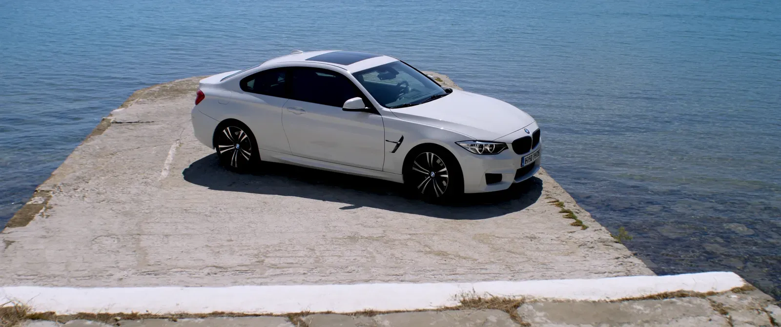 Weißes BMW Coupé an einer Uferpromenade am Meer